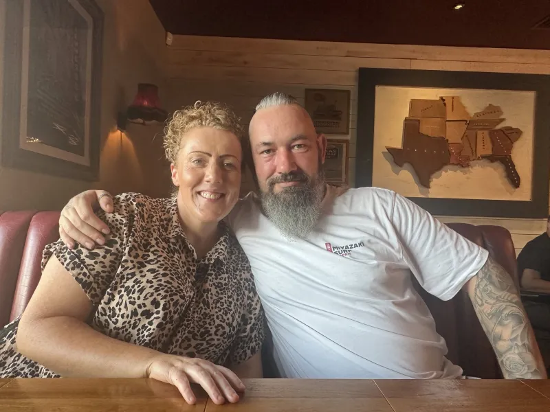 Nick and Vicky sitting together in a restaurant booth, smiling at the camera.